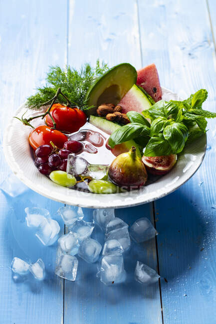 Tomatoes, fruits and basil on plate with ice cubes — Stock Photo