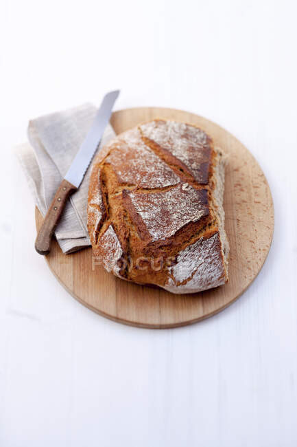 Pan de harina de trigo con un cuchillo de pan en una tabla de madera - foto de stock