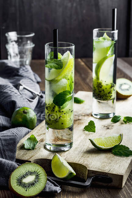 Cocktails au kiwi et au mojito au citron vert servis dans des verres sur une planche de bois avec des ingrédients — Photo de stock