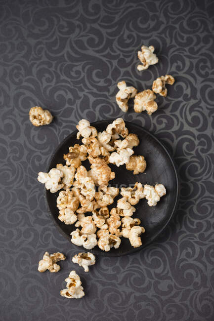 Gilded popcorn on a plate and a patterned tablecloth (seen from above) — Fotografia de Stock