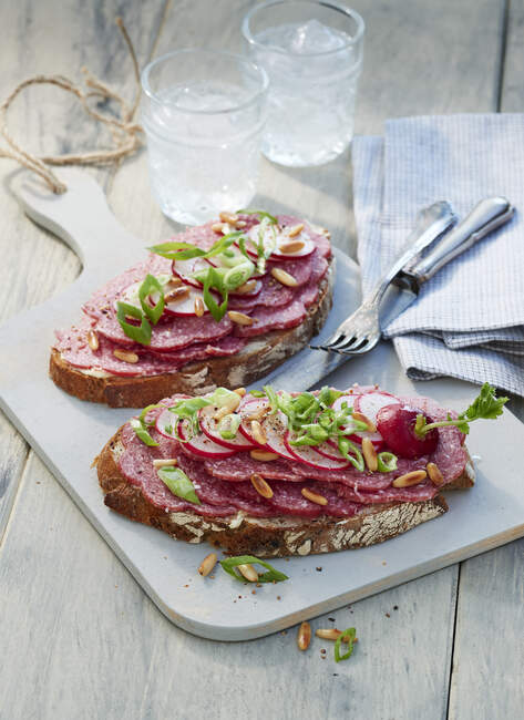 Two slices of bread with salami and herbs on light wooden board — Stock Photo