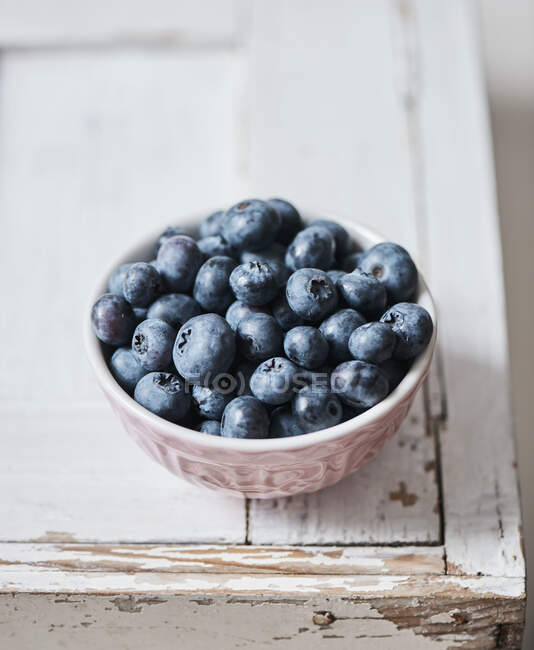 Fresh blueberries in ceramic bowl on white wooden surface — Stock Photo