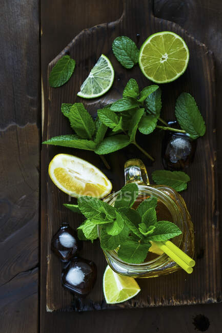 Té verde con lima, limón y menta en una jarra de vidrio sobre una tabla de madera - foto de stock
