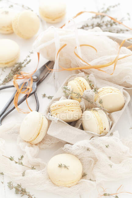 Macarons with thyme in gift box, scissors, textile and ribbon on table — Stock Photo