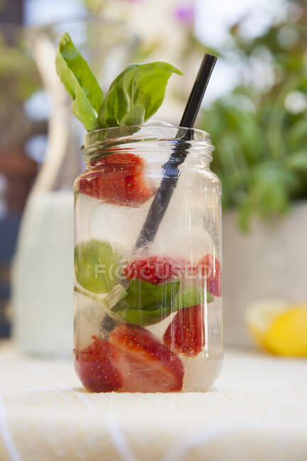 Lemonade with strawberries and basil in jar with straw — Stock Photo