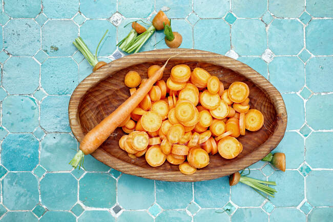 Whole and chopped fresh carrots in wooden bowl — Stock Photo