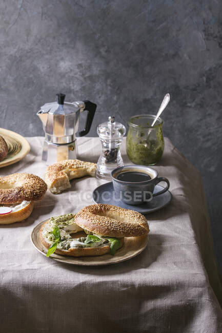 Café da manhã com bagel caseiro com sementes de gergelim, queijo creme e molho pesto, café na mesa — Fotografia de Stock