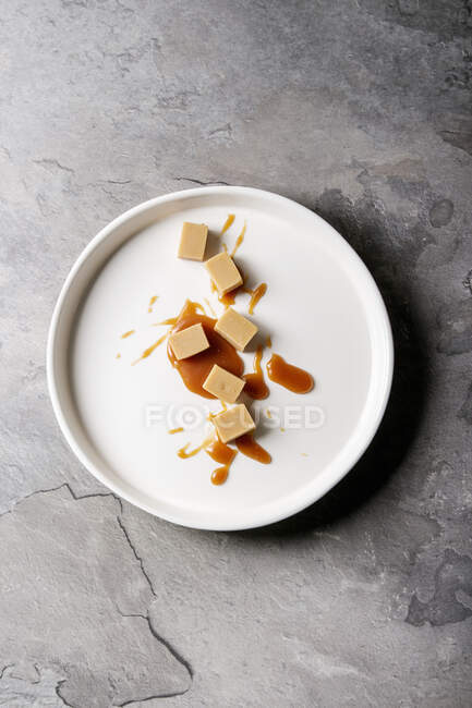 Salted caramel fudge candy with caramel sauce in white plate over grey texture background — Stock Photo