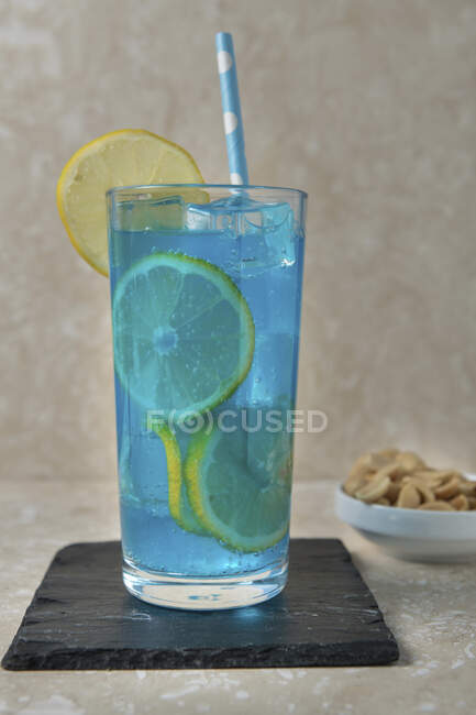 Cocktail alcool bleu avec tranches de citron et paille en verre — Photo de stock