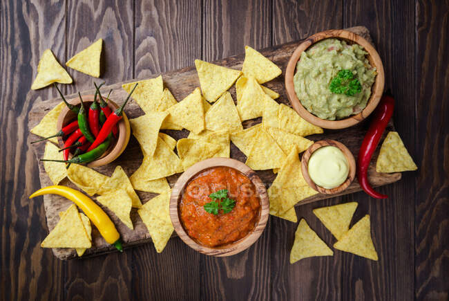 Nachos mexicanos com guacamole, salsa e molho de queijo em tigelas de madeira em fundo escuro — Fotografia de Stock
