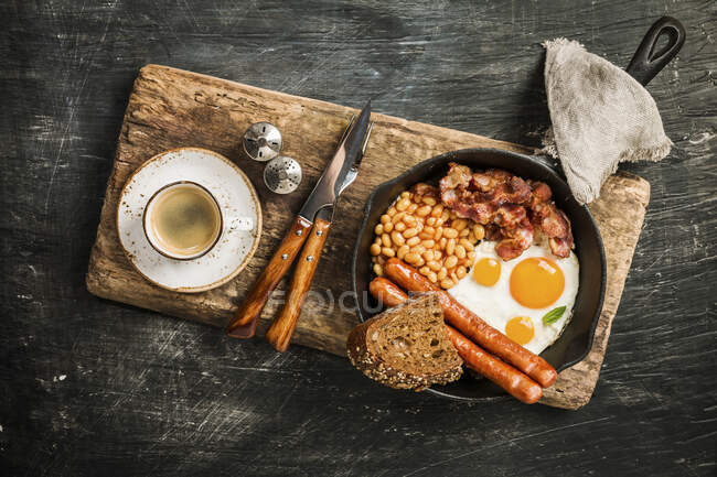 Huevos fritos, frijoles, tomates, salchichas, tocino y pan en sartén - foto de stock
