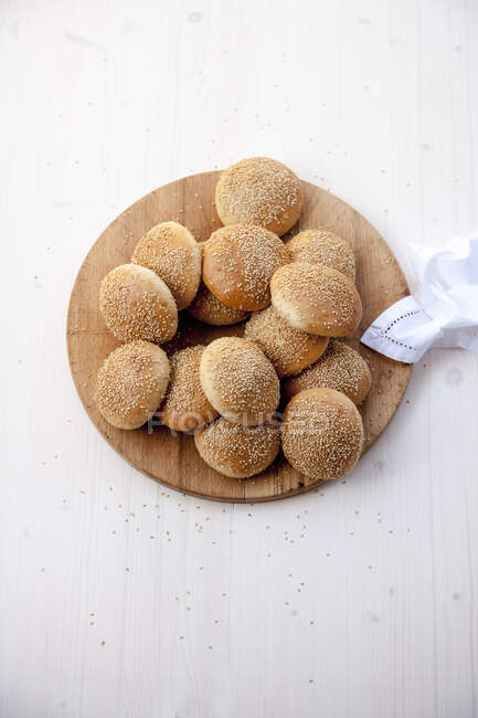 Petits pains au sésame, rouleaux de hamburger, sur une planche ronde en bois — Photo de stock