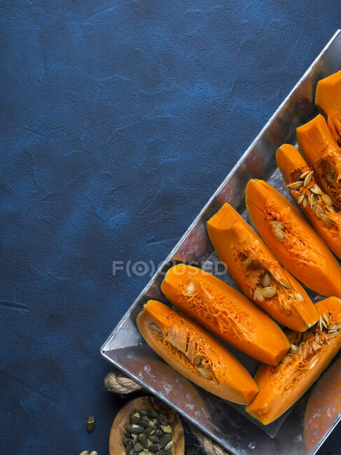 Raw sliced pumpkin ready to be cooked on a tray over blue background — Stock Photo