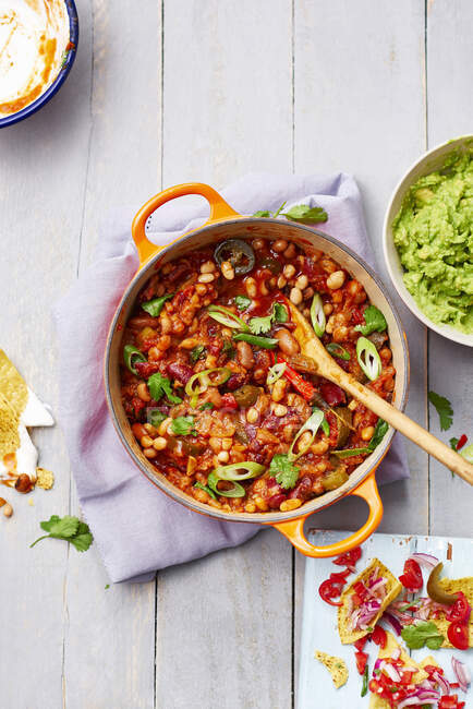 Vegetarian bean chili topped with spring onions, chili and coriander, served with tortilla chips with raw onion and fresh chili and guacamole — Stock Photo