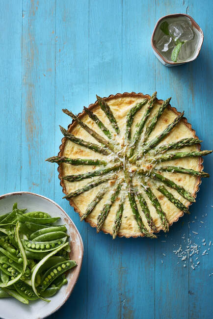 Asparagus tart with grated cheese sprinkled across top and served with fresh garden peas — Stock Photo