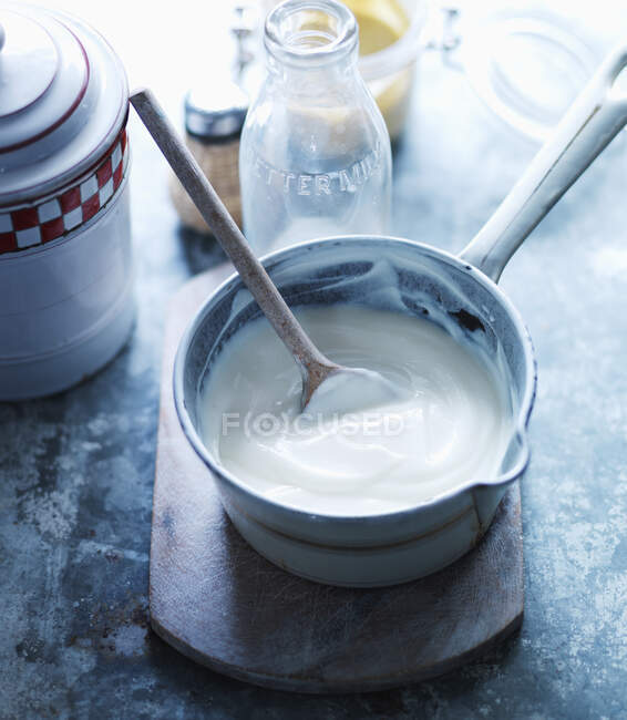 Bechamel sauce with a wooden spoon in a saucepan — Stock Photo