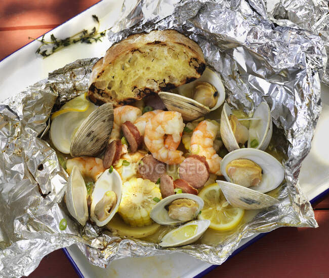 Seafood cooked in foil with corn on the cob and grilled bread — Stock Photo