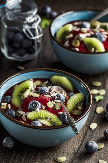 Bowl of berries smoothie with fresh blueberries, kiwi, pumpkin and sunflower seeds on top — Stock Photo