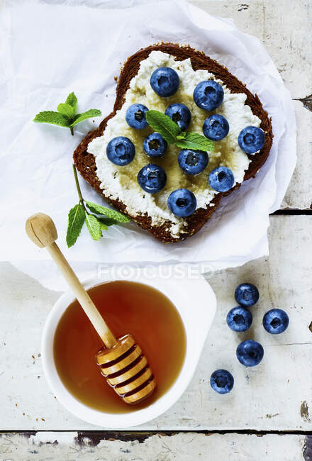 Close up of grunge white wooden table with ricotta, fresh blueberries and honey sandwich on whole grain bread — Stock Photo