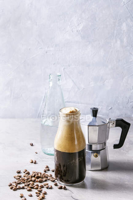 Bottle of fizzy iced Coffee espresso with bottle of sparkling water, coffee maker and roasted beans over grey table — Stock Photo