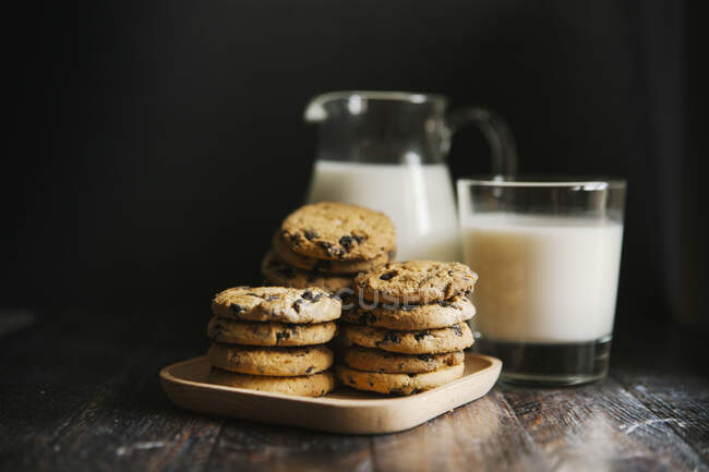 Stacks of cookies with chocolate and milk in glass and pitcher — Stock Photo