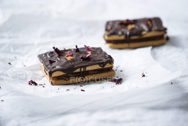 Biscuits with cocoa cream, chocolate icing and dried rose petals — Stock Photo