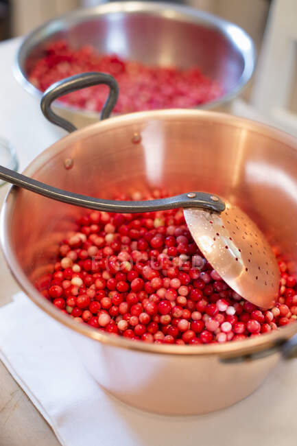 Lingon berry jam being made, raw lingon berries in a pot with a draining spoon — Stock Photo