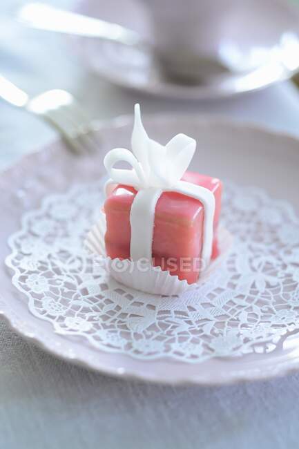 A pink petit four on a paper doily — Stock Photo