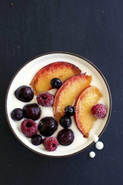 Fruit bowl with peaches, raspberries and cherries on natural yoghurt — Stock Photo
