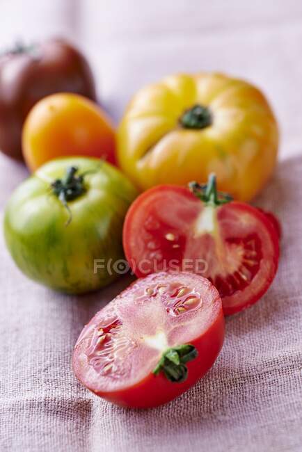 Varios tomates coloreados en un paño de lino, uno reducido a la mitad - foto de stock