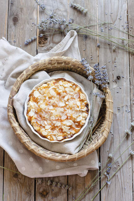 Tarta de tarta con albaricoques y hojuelas de almendras en lata en cesta con paño y flores secas de lavanda en la mesa - foto de stock
