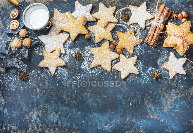 Biscoitos em forma de estrela de Natal de gengibre com canela, anis, nozes, moldes de cozimento e açúcar em pó em contraplacado escuro fundo pintado — Fotografia de Stock