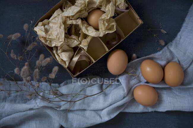 Caja de papel con huevos en tela azul y rama esponjosa - foto de stock