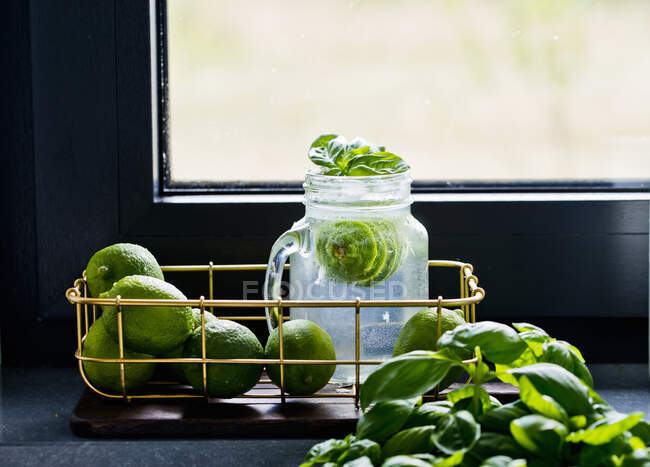 Lemonade with whole limes and basil leaves — Stock Photo