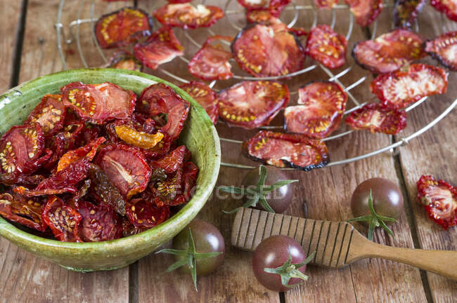 Dried tomatoes on a wire rack and in a ceramic bowl — Stock Photo