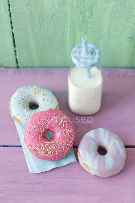 Beignets avec un glaçage coloré au sucre et une bouteille de lait — Photo de stock
