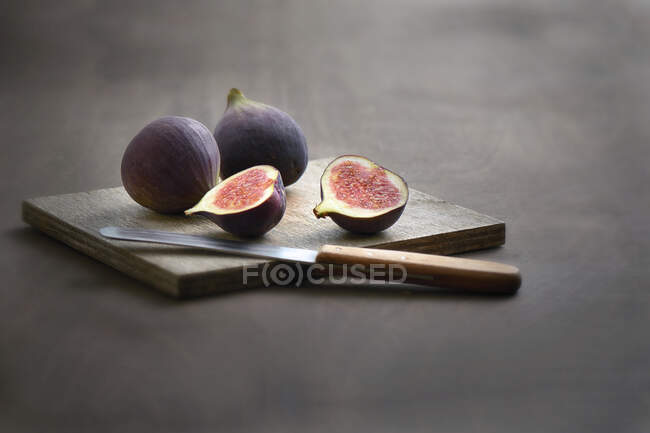 Свежие инжиры на деревянной доске с маленьким фруктовым ножом — стоковое фото