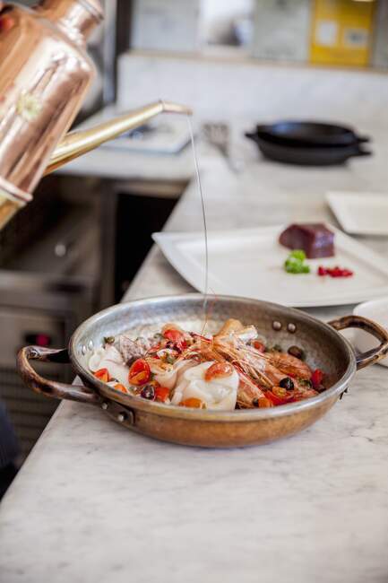 Креветки, кальмари та вишневі помідори з олією на мідній сковороді — стокове фото