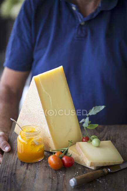 Um homem segurando uma tábua de queijo com tomates e um pote de geléia — Fotografia de Stock