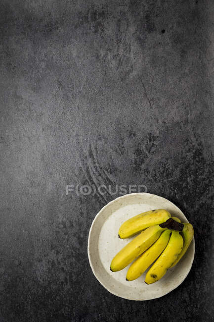 Small bananas on a white plate at a black backdrop — Stock Photo