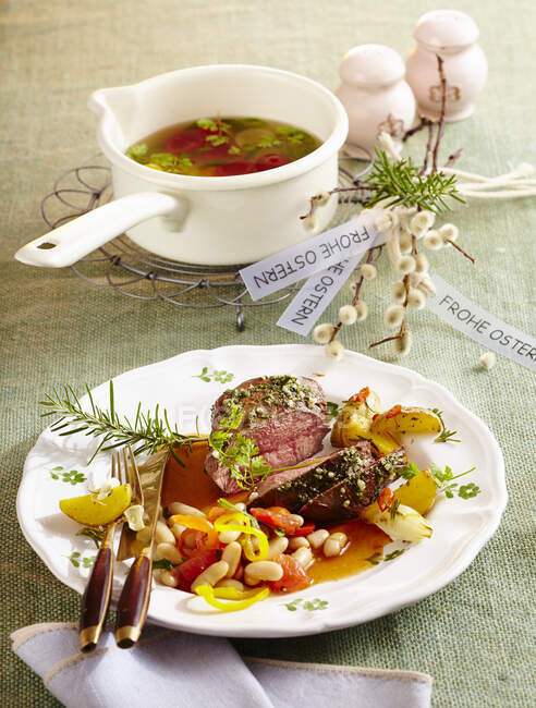 Tomato essence with cherry tomatoes and roasted lamb flank with herb potatoes and white beans for Easter — Stock Photo