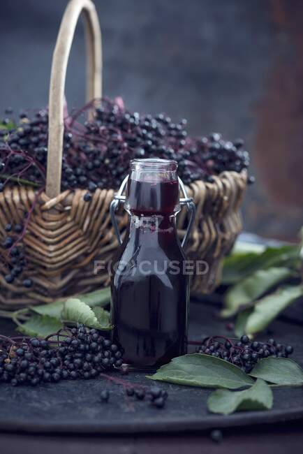Black elderberries in basket and bottle of syrup — Stock Photo