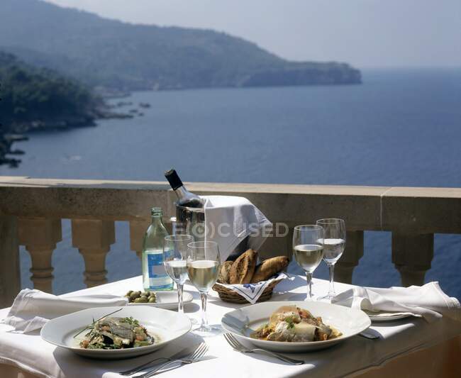 Platos de pescado y vino en mesa con vistas al mar - foto de stock