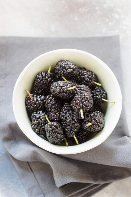 Fresh mulberries in small bowl on gray cloth — Stock Photo