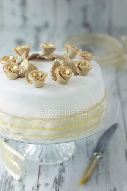 Un gâteau de fête blanc avec des roses dorées et un ruban décoratif — Photo de stock