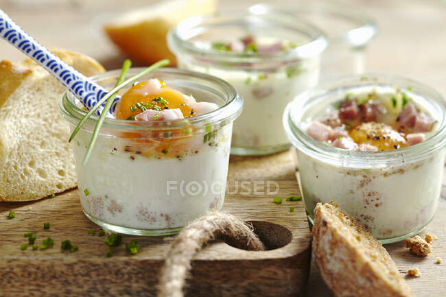 Eggs in mini jars with chives and ham on wooden board — Stock Photo
