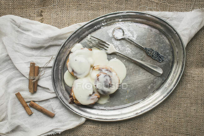 Cinnamon rolls with cream-cheese icing and cinnamon sticks on a silver dish — Stock Photo