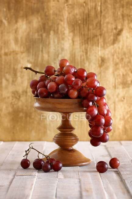 Uvas rojas sobre soporte de madera y sobre superficie de madera — Stock Photo