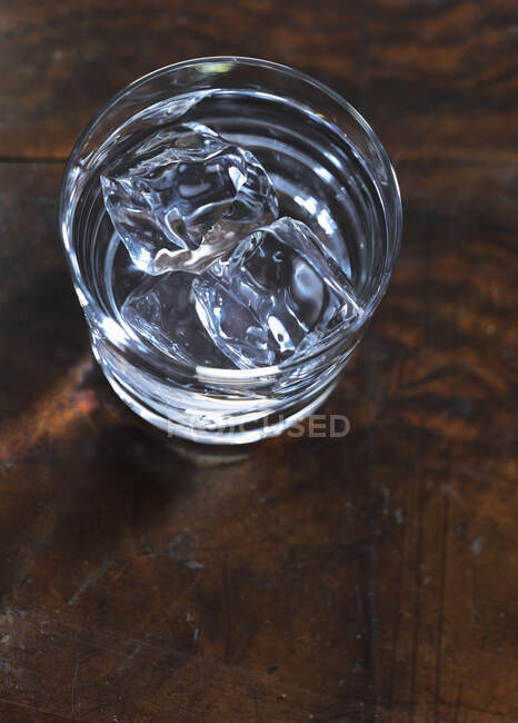 Vaso de agua con hielo en superficie de madera - foto de stock