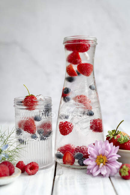 Agua con bayas frescas y cubitos de hielo en frasco y botella - foto de stock